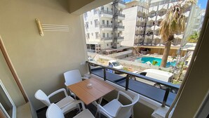 Un balcón con una mesa y cuatro sillas, con vista a una piscina y edificios.