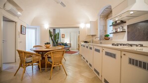 A kitchen with a dining area, white cabinets, a ceiling fan, and a dining table with wicker chairs.