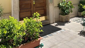 La entrada de un edificio con una puerta de madera grande, un toldo de metal y plantas en macetas.