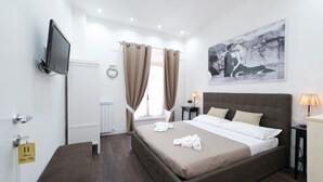 Habitación de hotel con cama, televisión montada en la pared, un cuadro y una ventana con cortinas.