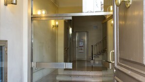 Entrada de hotel con puerta de cristal, alfombra roja y escalera que lleva a los pisos superiores.