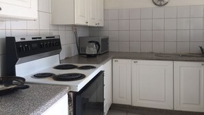 Una cocina con armarios blancos, estufa, microondas y hervidor.
