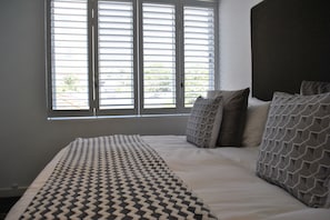 A bedroom with a large bed, a patterned throw blanket, and a view through a window with blinds.