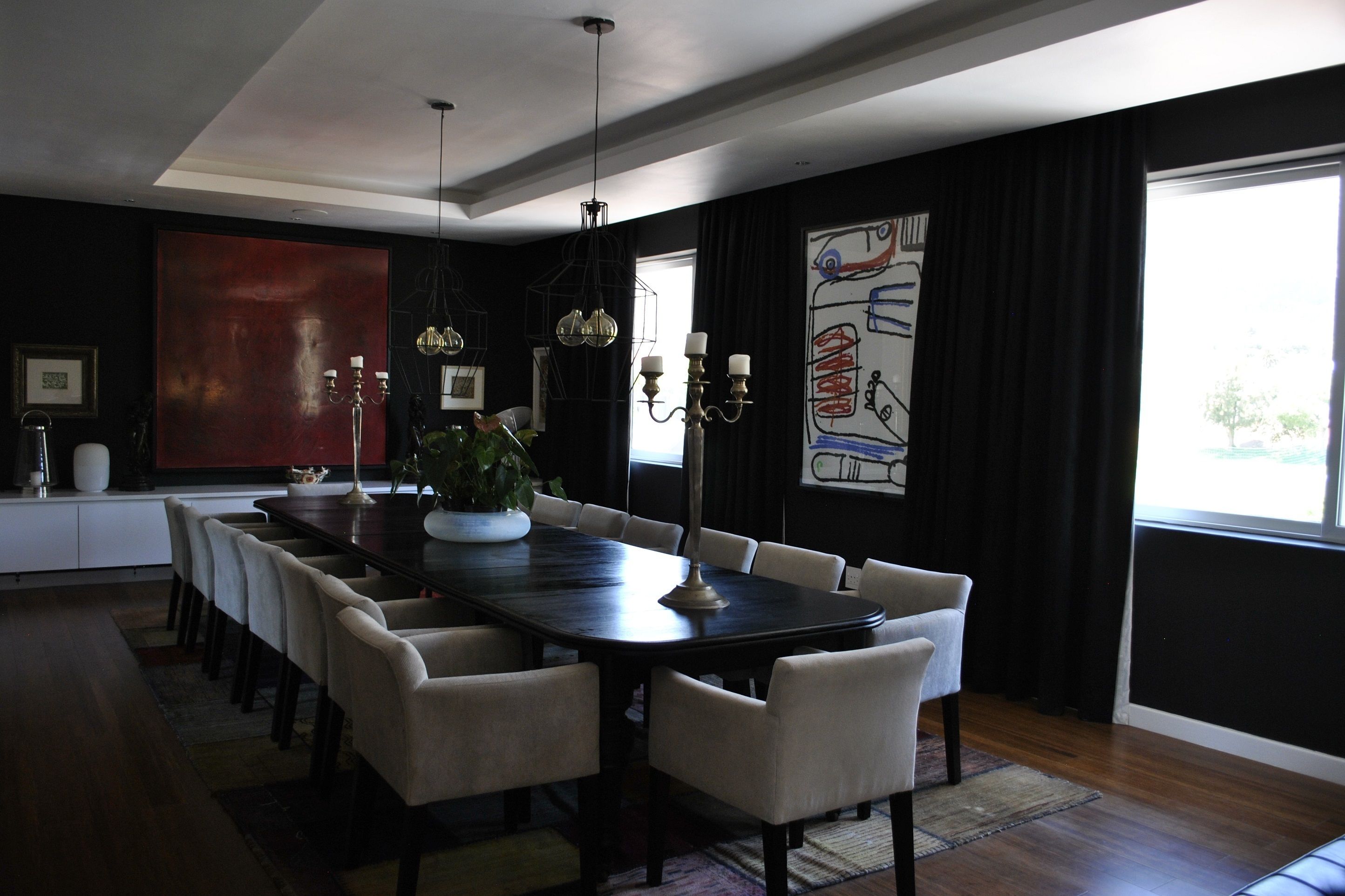 A modern dining room with a long table, white chairs, a chandelier, and artwork on the walls.