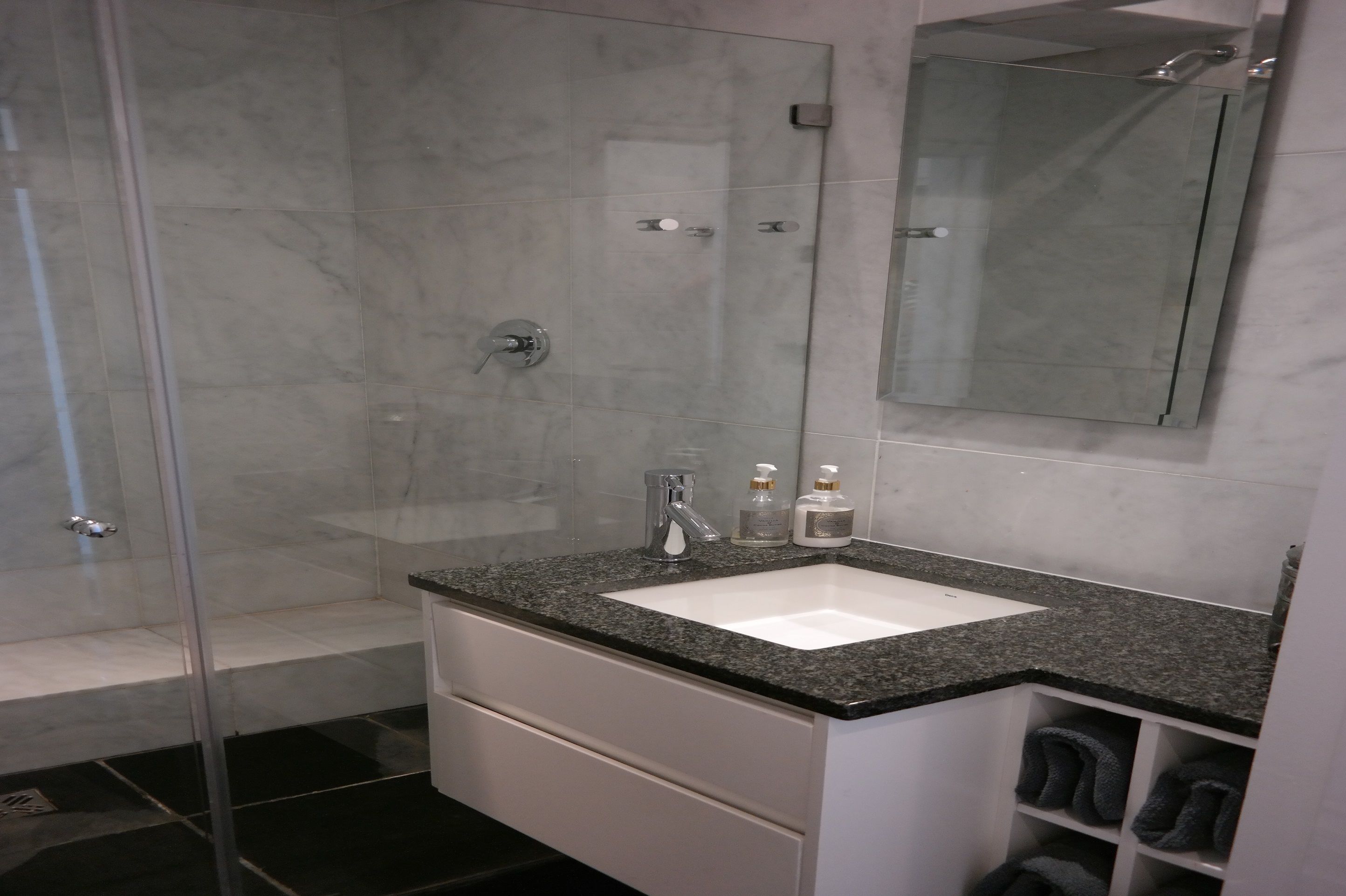 A modern bathroom with a glass-enclosed shower, a white sink with a granite countertop, and a mirror above the sink.