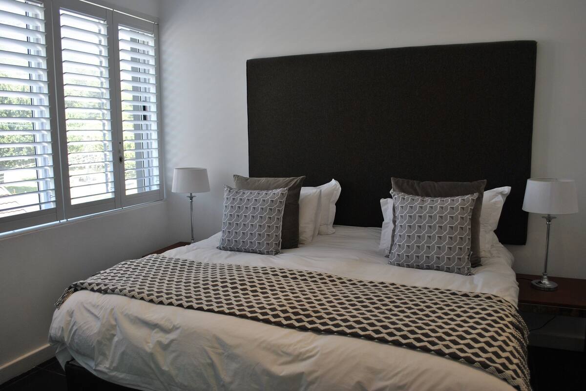 A neatly made bed with a patterned bedspread, two pillows, and two bedside lamps.