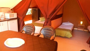 A tented accommodation with a bed, a table with chairs, a microwave, and a small bedside table with a lamp. - Camping Baalse Hei (Turnhout)