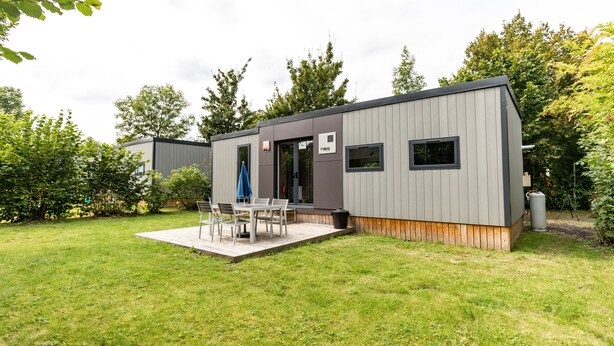 A modern, single-story building with a patio area featuring a table and chairs. - Camping Baalse Hei (Turnhout)