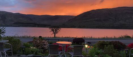 A patio with outdoor seating and a view of a lake and mountains during sunset.