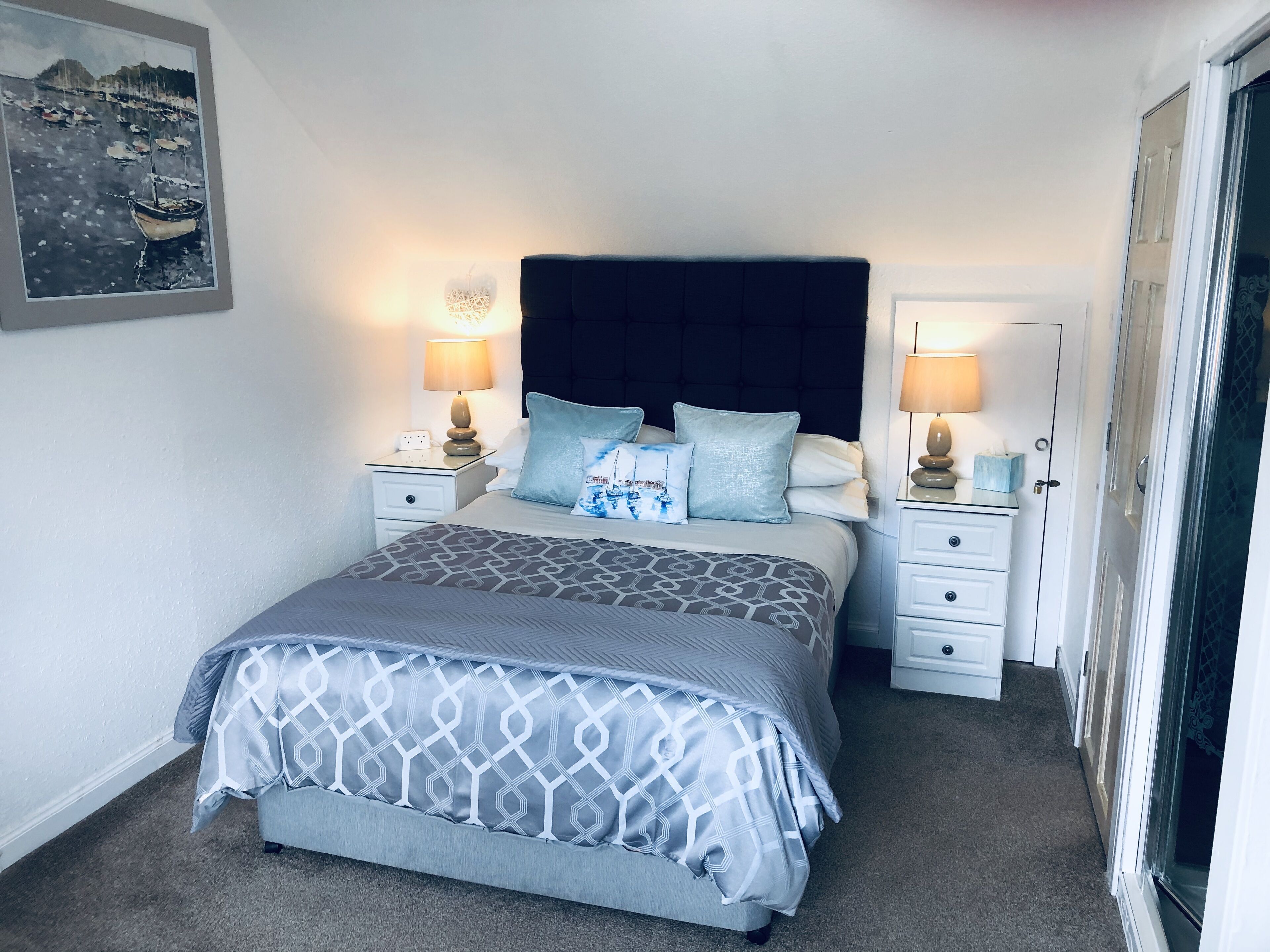 A neatly arranged bedroom with a bed, two bedside tables, a nightstand, and a door.