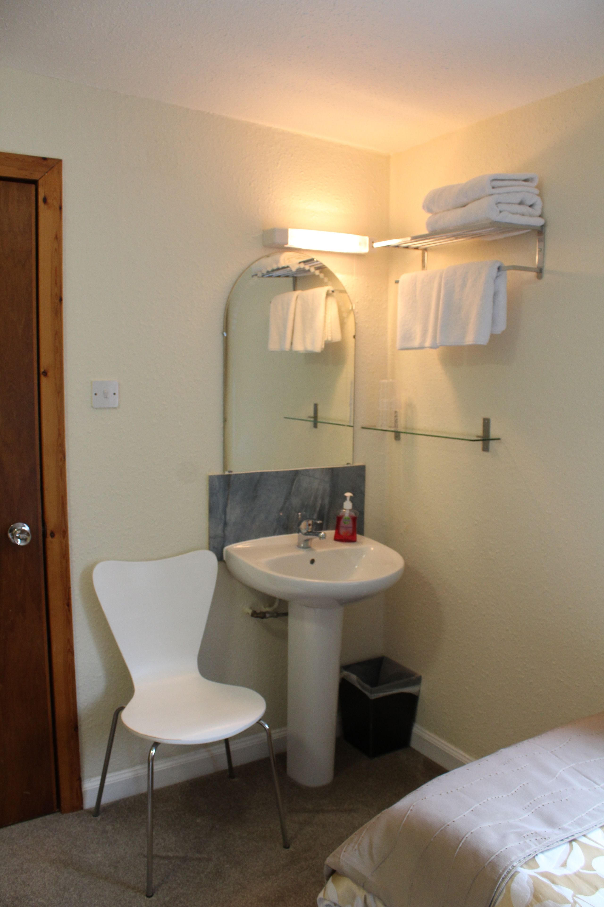 A bathroom with a white sink, a mirror, a towel rack, a white chair, and a door.