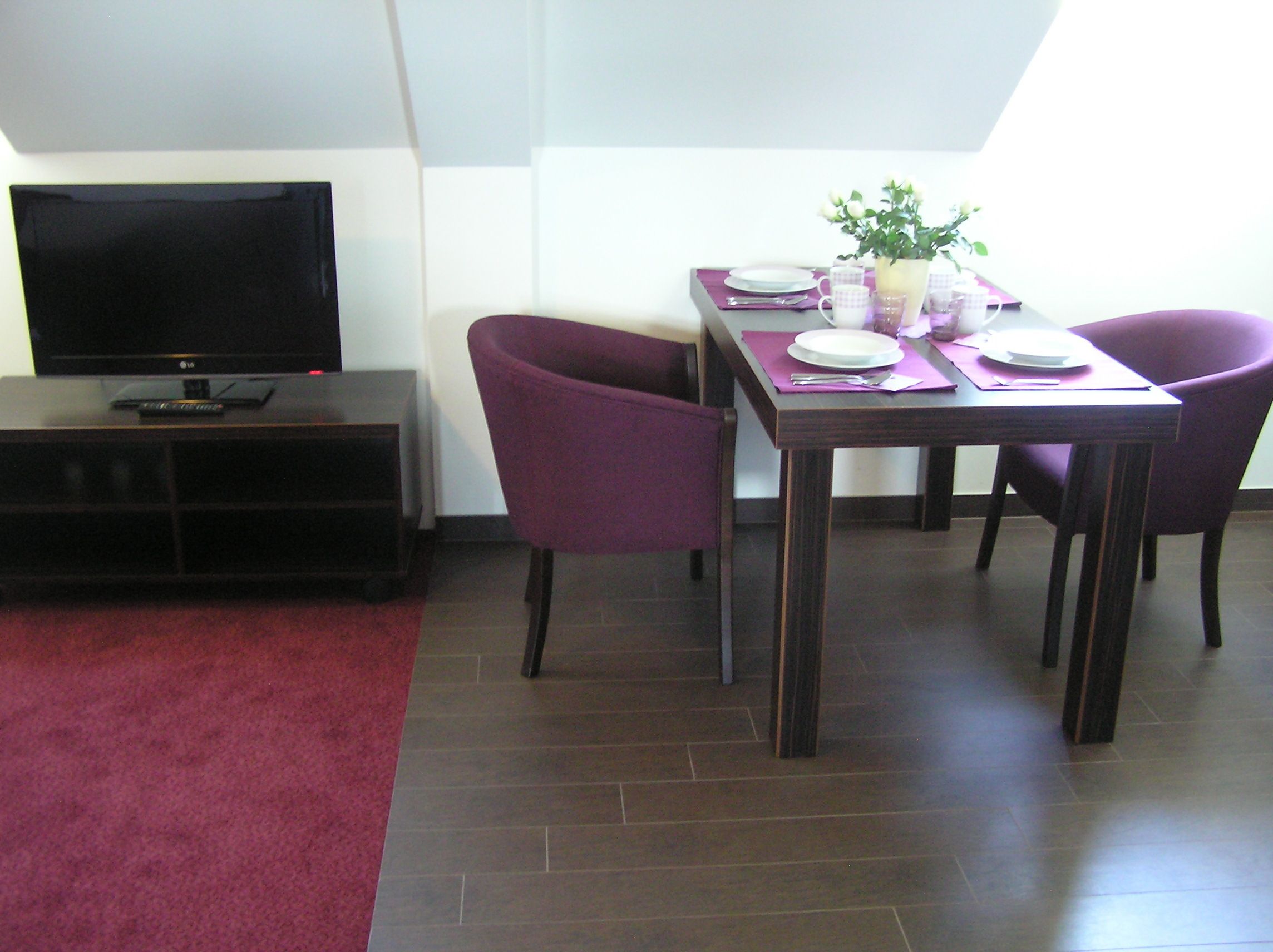 A dining area with a table set for four, two purple chairs, a flat-screen TV, and a dark wood floor.