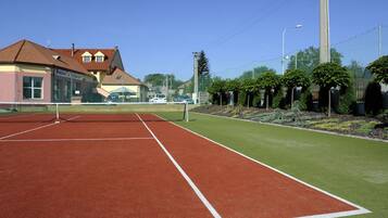 Een tennisbaan met een net, omringd door een hek en bomen.