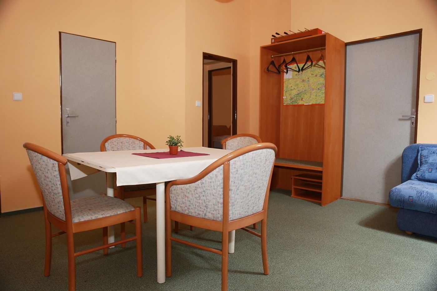Um quarto pequeno com uma mesa de jantar, quatro cadeiras, um cabideiro e um sofá azul.