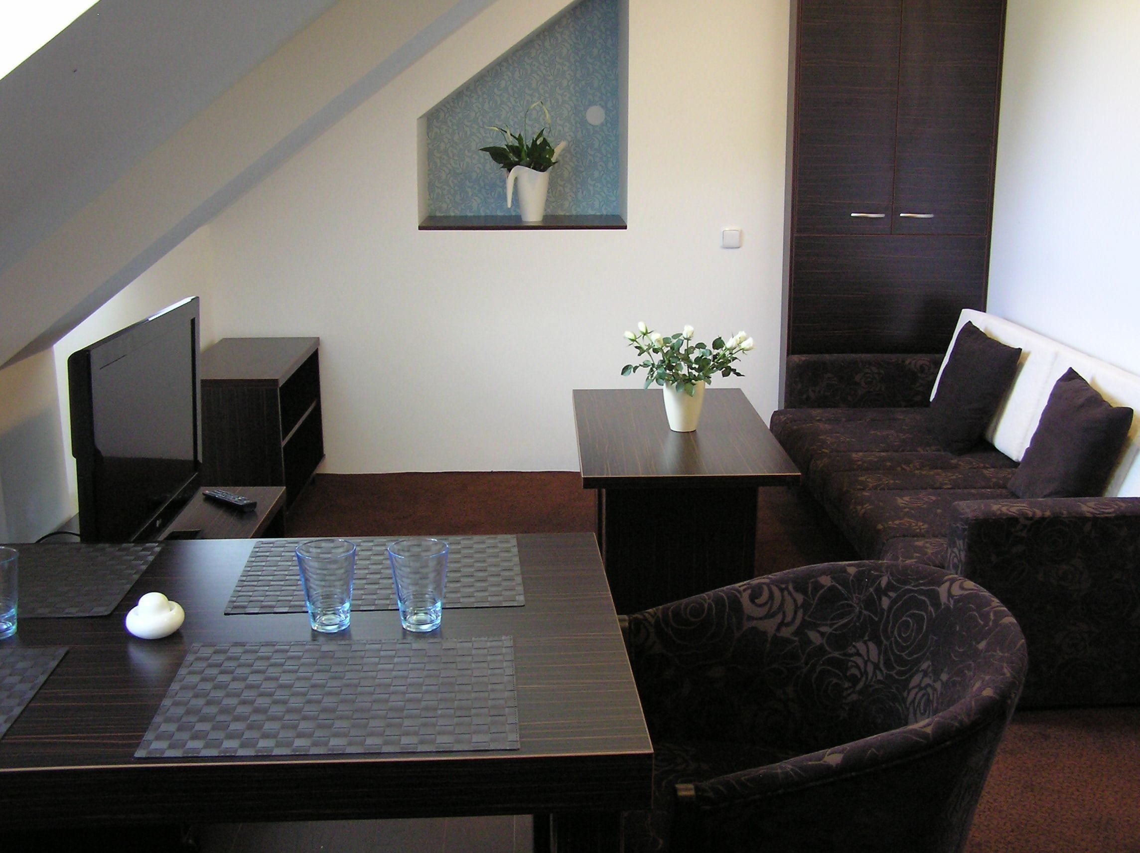 A modern living room with a dark brown sofa, a small table with a potted plant, a TV, and a remote control.