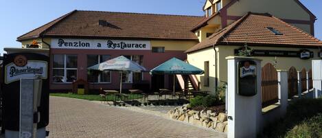 A building with a sign reading "Penzion a Restaurant" and outdoor seating with umbrellas.