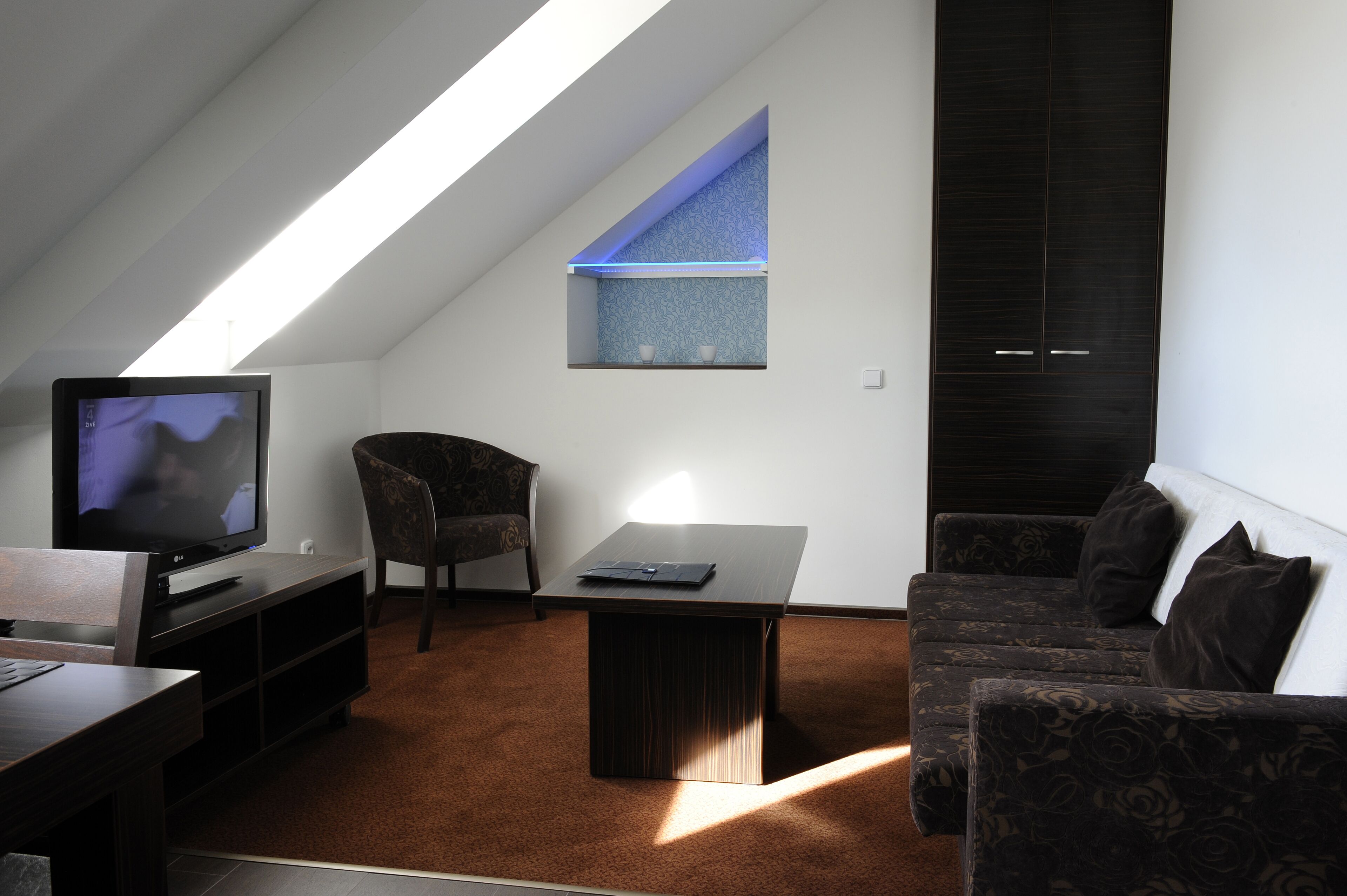 Ein modernes Wohnzimmer mit Fernseher, einer Couch, einem Couchtisch und einem kleinen Fenster mit blauem Licht.