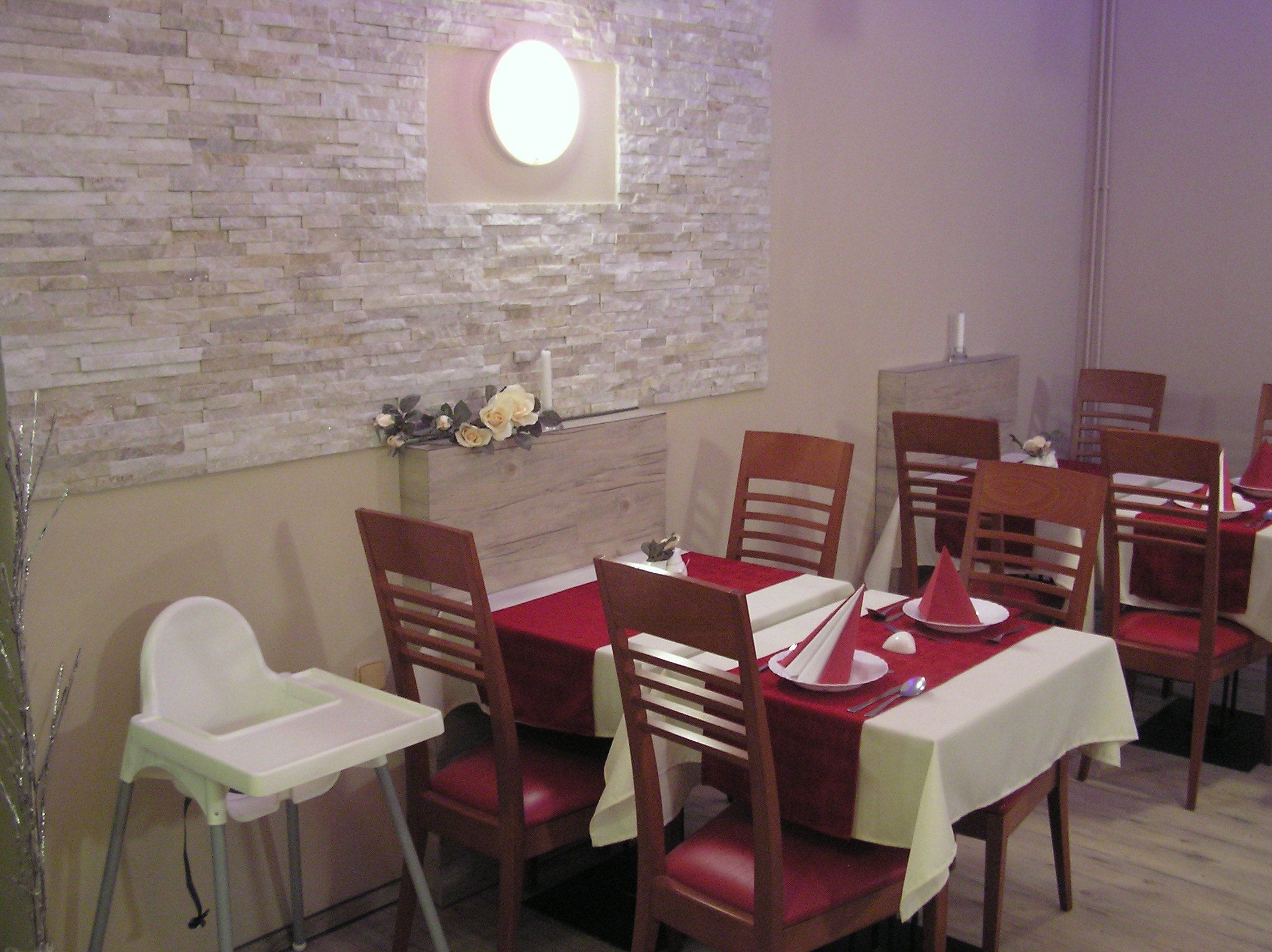 Un comedor con pared de ladrillo, una lámpara redonda y sillas y mesas de madera.