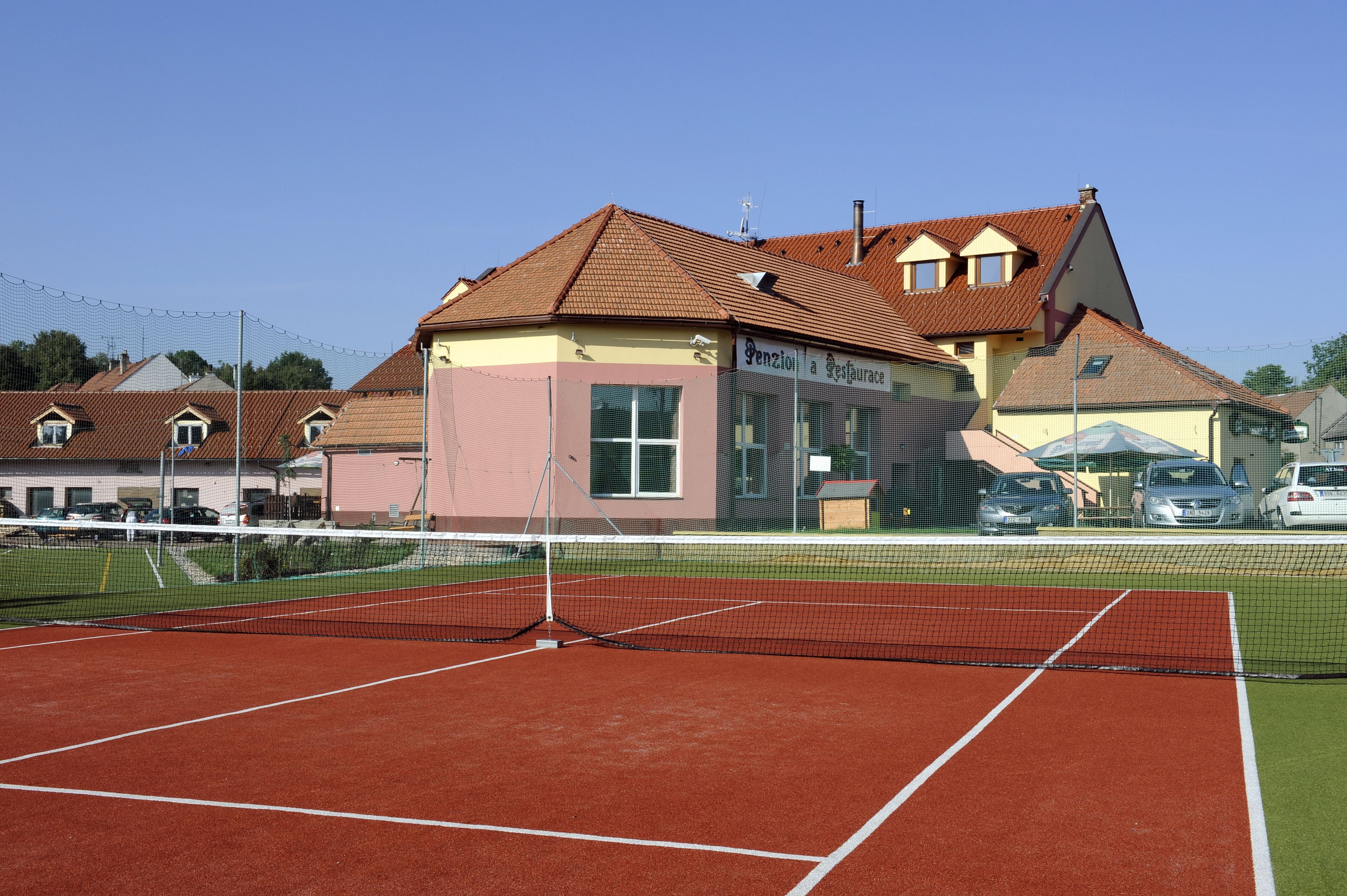 A tennis court with a net, surrounded by buildings and parked cars.