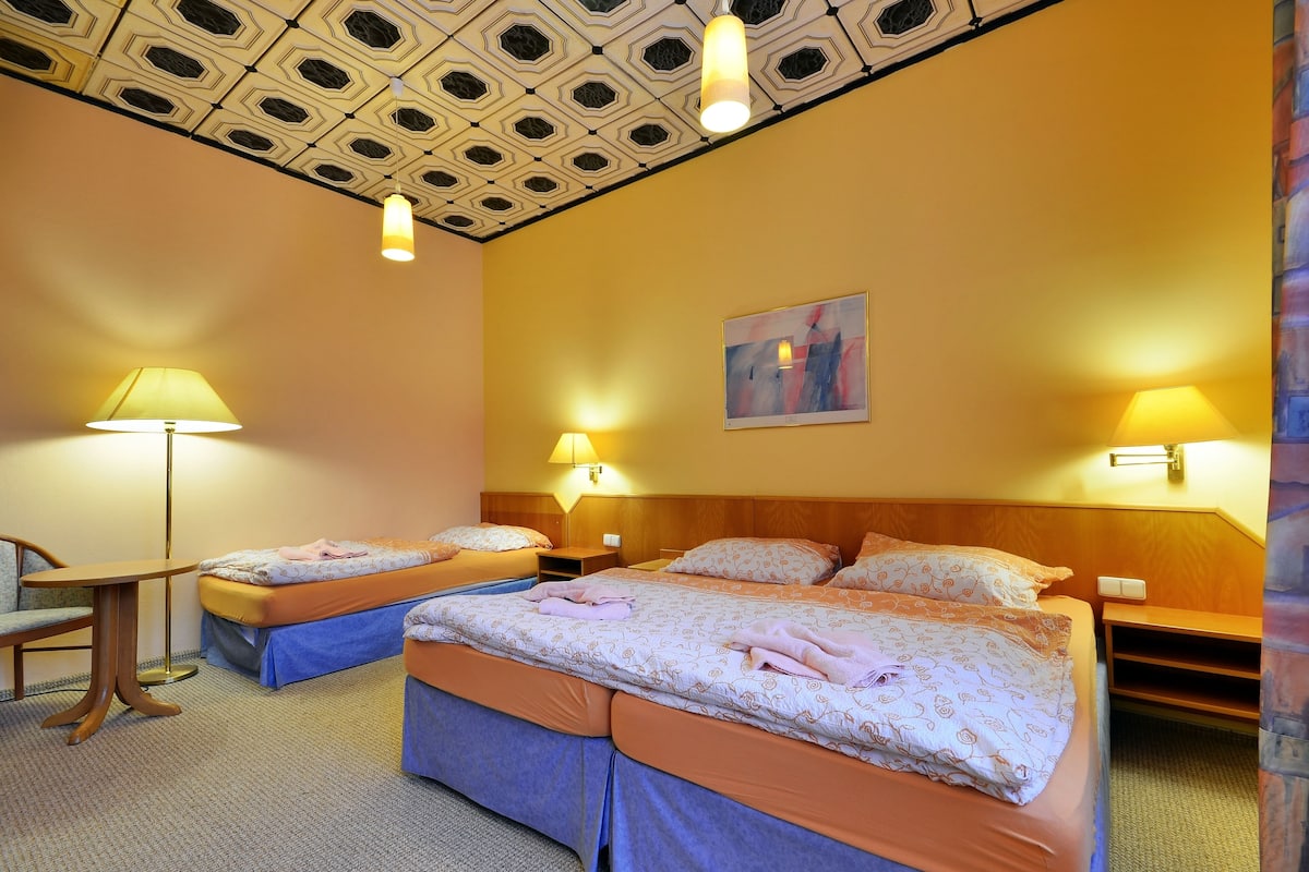 Une chambre d’hôtel avec deux lits, un bureau et une chaise. On y trouve des lampes fixées au mur et un luminaire au plafond.