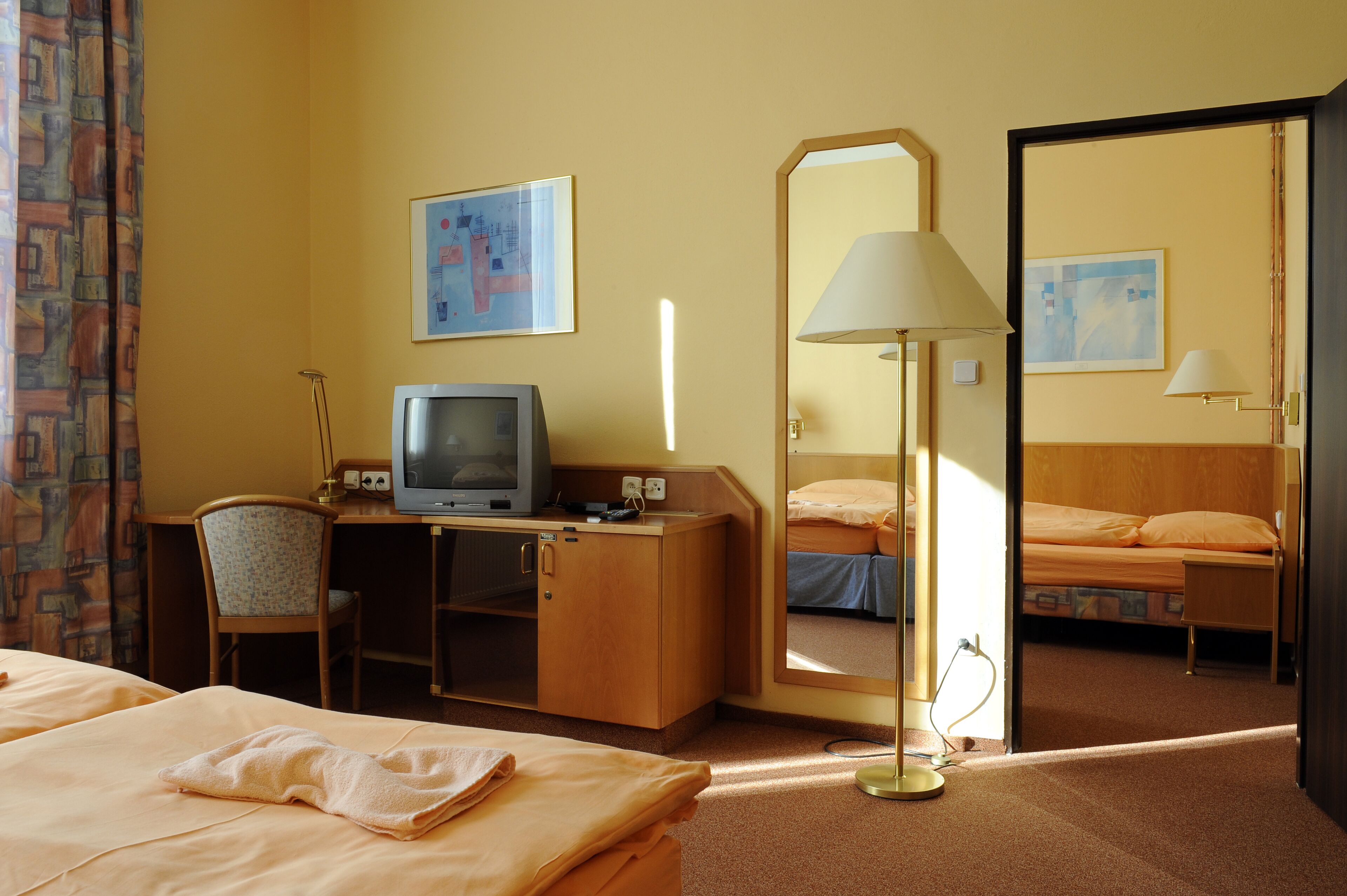 A hotel room with a bed, desk, television, and a mirror.