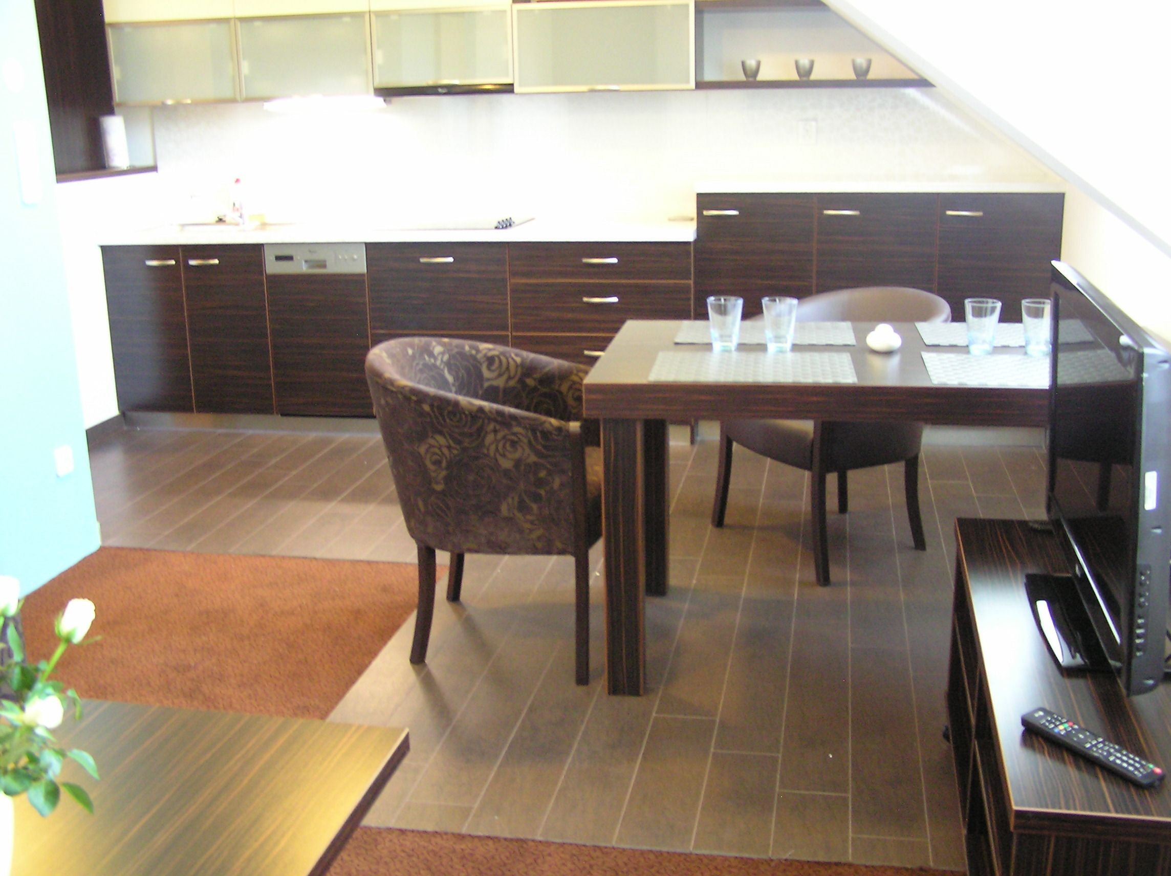 Una cocina moderna con armarios de madera oscura, una mesa de comedor con sillas y un control remoto sobre una mesita auxiliar.