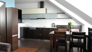 Una cocina moderna con armarios oscuros, una zona de comedor con mesa y sillas de madera, y un techo inclinado con tragaluces.
