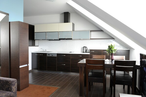 A modern kitchen with dark cabinetry, a dining area with a wooden table and chairs, and a sloped ceiling with skylight.