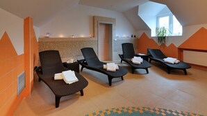 Un cuarto de spa con cuatro sillones oscuros de mimbre, suelo de baldosas, alfombra de diseño geométrico y tragaluz.