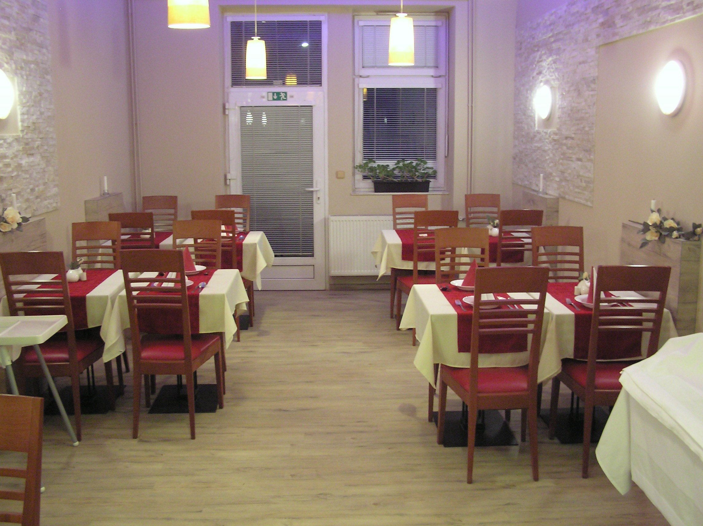 Un coin repas avec des tables disposées pour accueillir quatre personnes, des chaises en bois et une plante en pot près de la fenêtre.