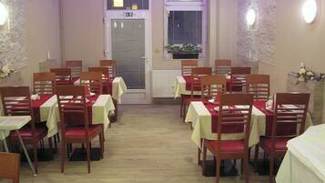 A dining area with tables set for four, wooden chairs, and a potted plant by the window.