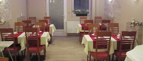Un coin repas avec des tables disposées pour accueillir quatre personnes, des chaises en bois et une plante en pot près de la fenêtre.