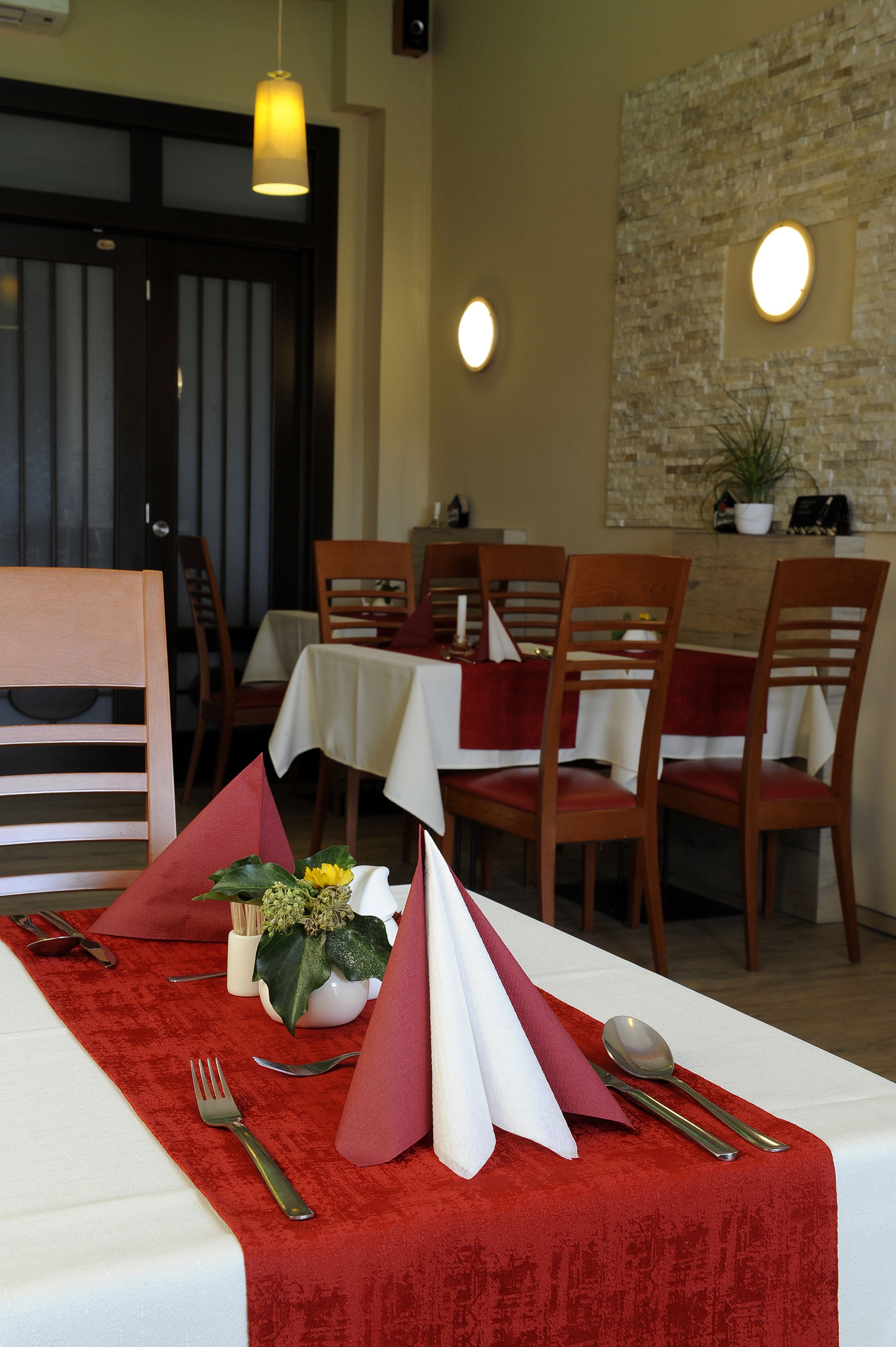 A dining area with tables set for four, each with a white tablecloth and red napkins.