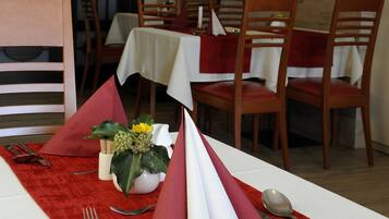 A dining area with tables set for four, each with a white tablecloth and red napkins.