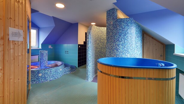 Un moderno spa con una pared de mosaico azul, una bañera de madera y una pequeña zona de estar.