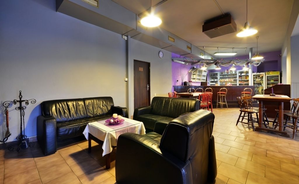 Un rincón de descanso acogedor con sofás de cuero, una mesita con mantel morado y una zona de bar con taburetes y estantes llenos de botellas.