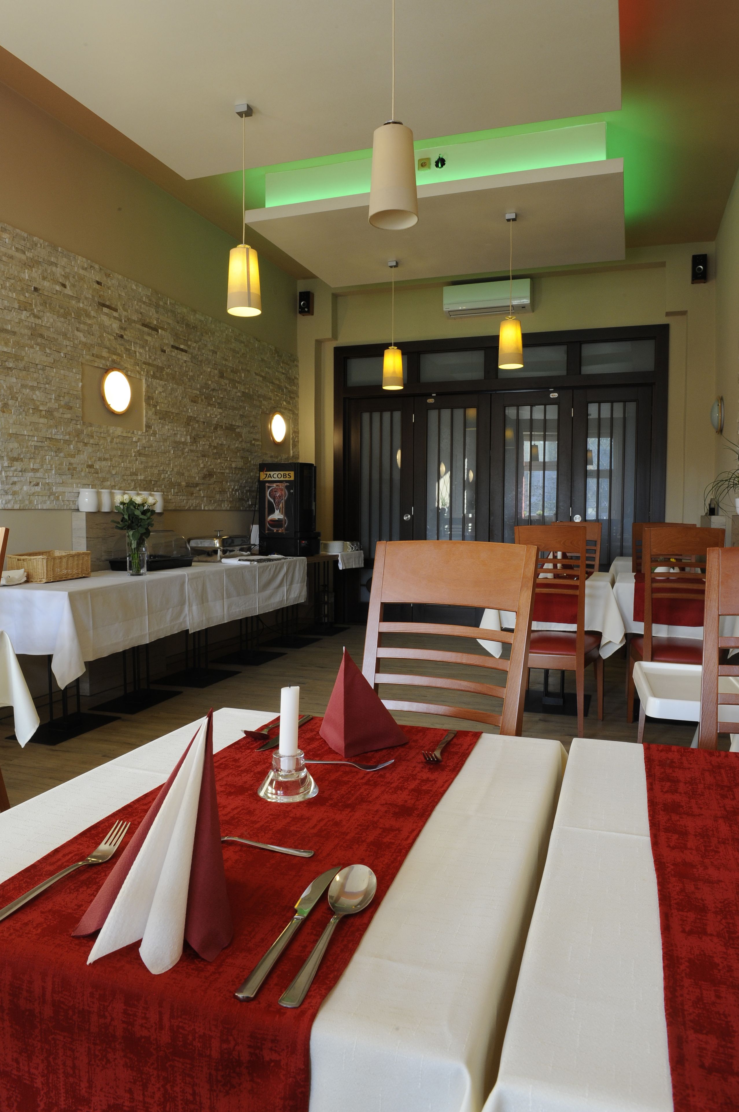A restaurant with a brick wall, wooden chairs, and tables set with white tablecloths and red napkins.