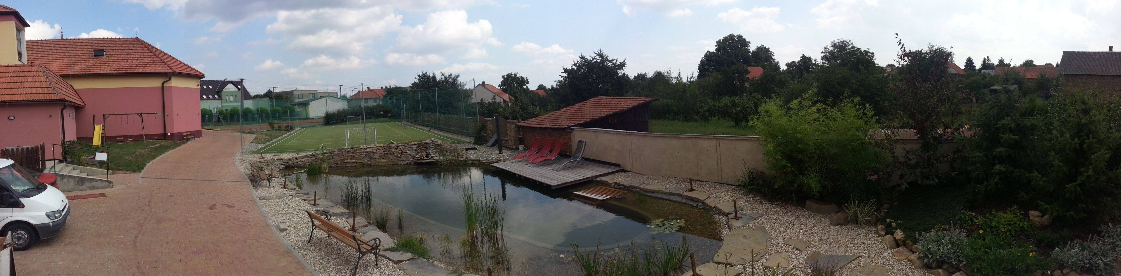 Ein Wohngebiet mit einem kleinen Teich, einem Tennisplatz und einem Weg zu einem geparkten Auto.