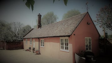 A single-story house with a tiled roof, a chimney, and a small porch area with potted plants.