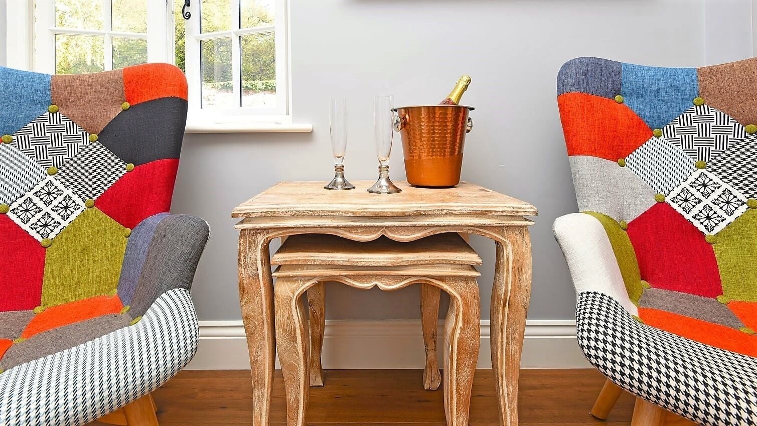 Een kamer met twee kleurrijke fauteuils, een houten tafel en een koperen emmer met glazen en een fles.