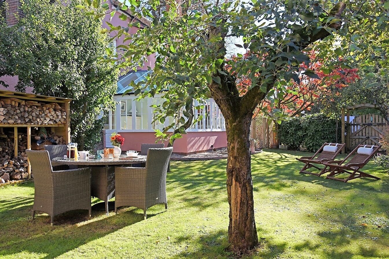 Un patio con mobiliario de mimbre, una mesa con bebidas y un árbol en el centro.