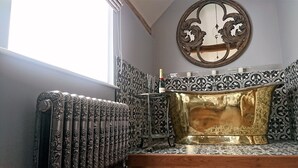 Un baño con radiador, bañera dorada y azulejos estampados.