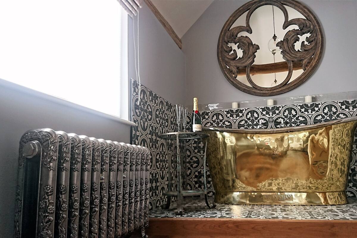 Un baño con radiador, bañera dorada y azulejos estampados.