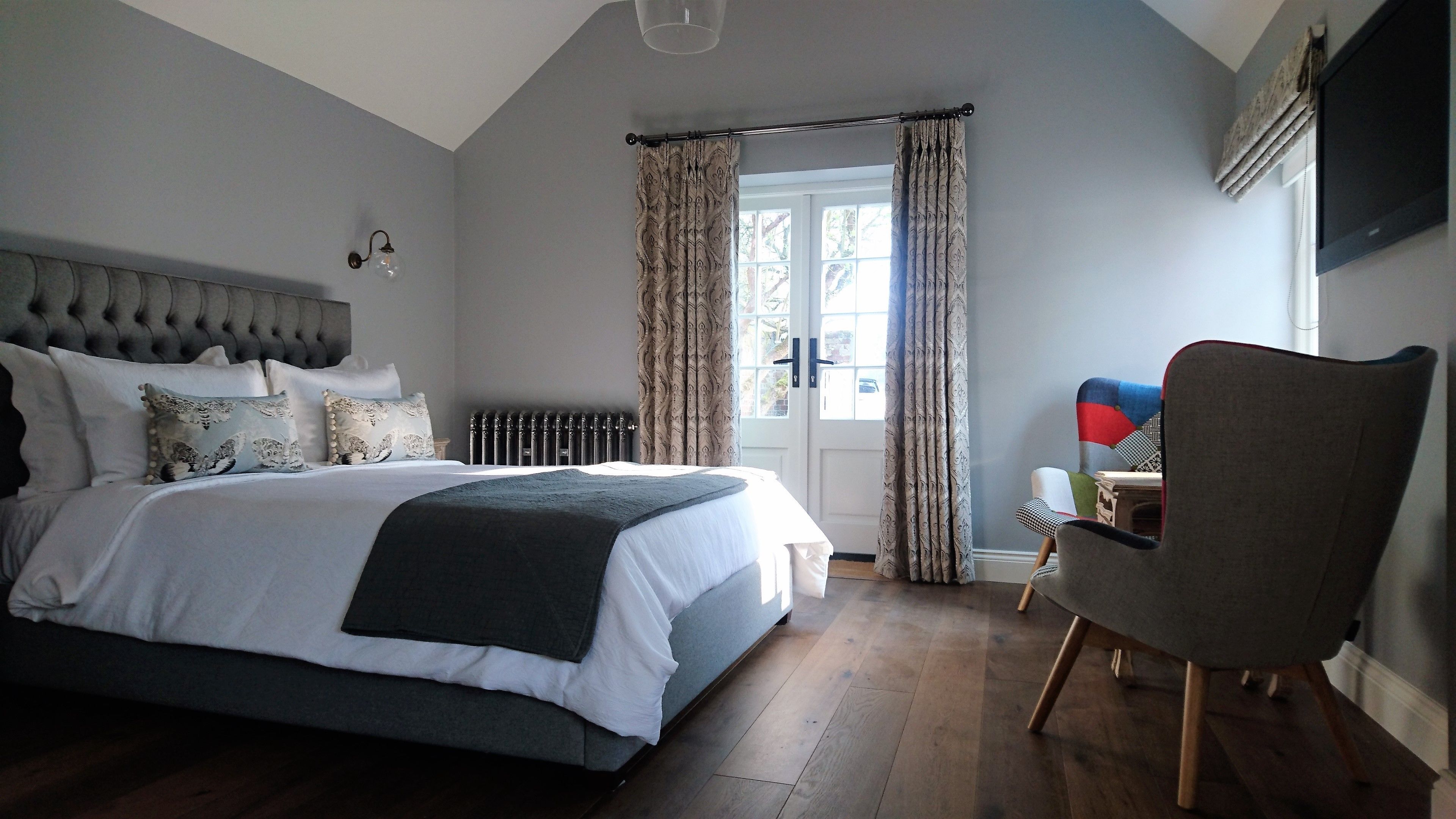A bedroom with a large bed, a chair, a radiator, and a window with curtains.