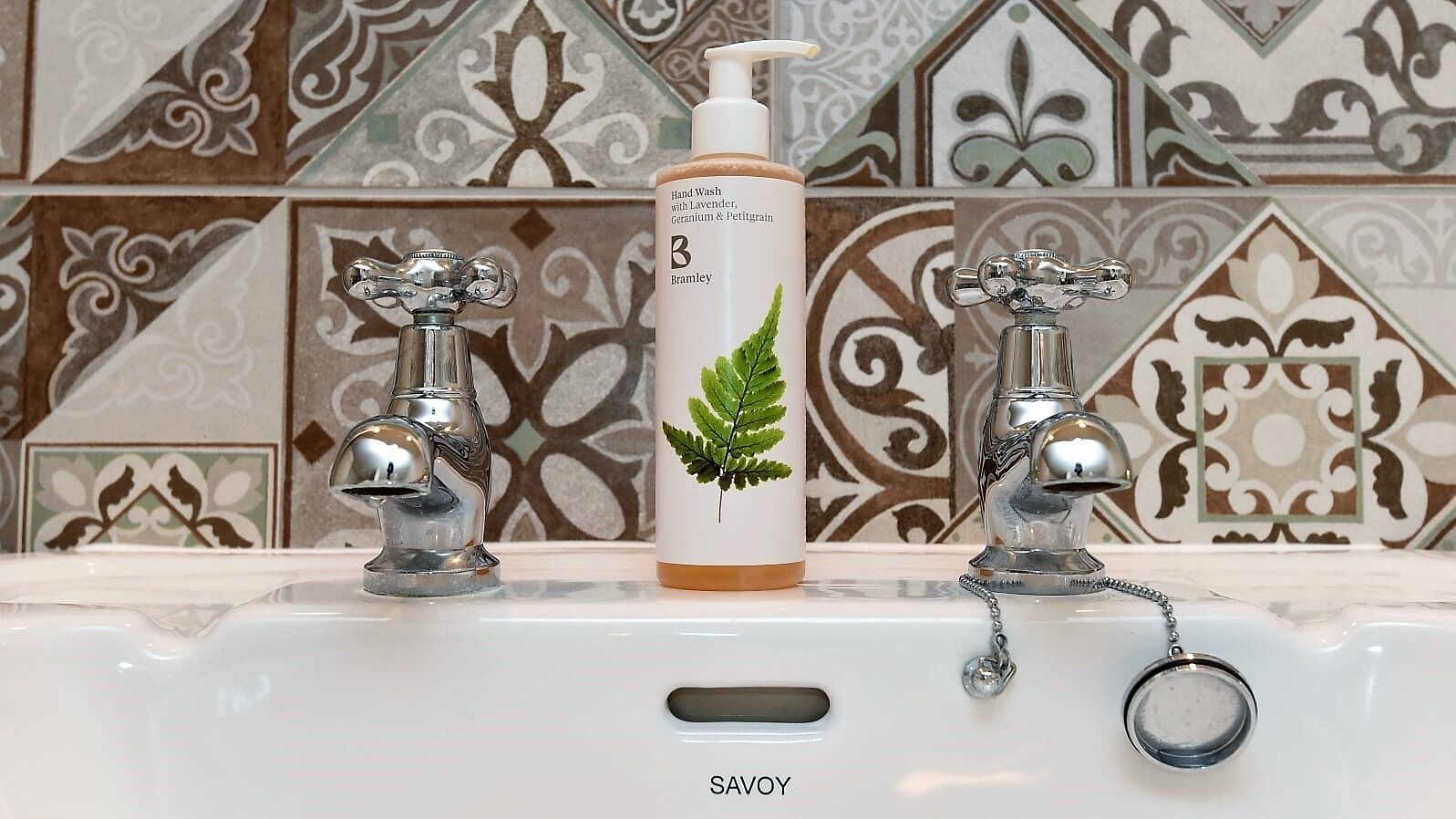 Un bagno con un lavandino bianco, due rubinetti cromati e una bottiglia di sapone per le mani con un motivo a foglia.