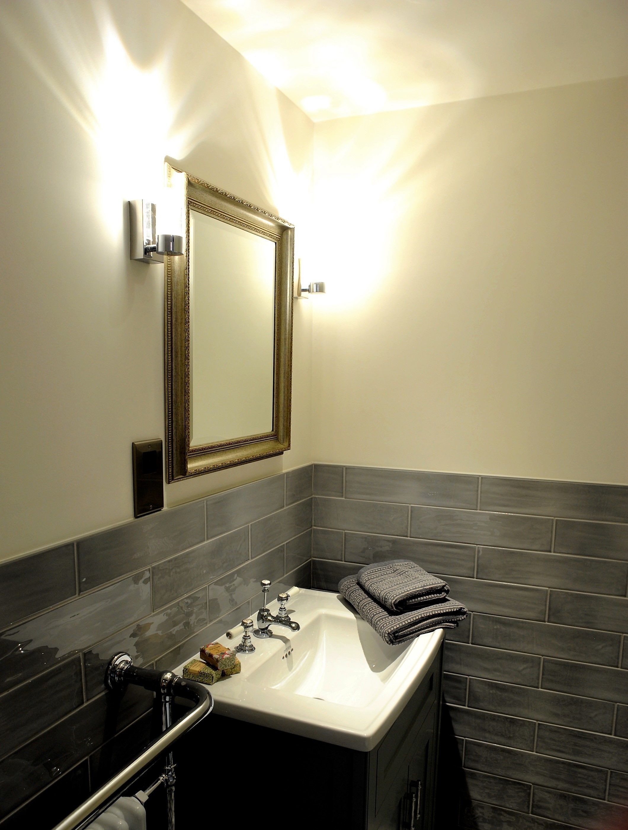 A bathroom with a white sink, a mirror with a gold frame, and dark grey tiled walls.