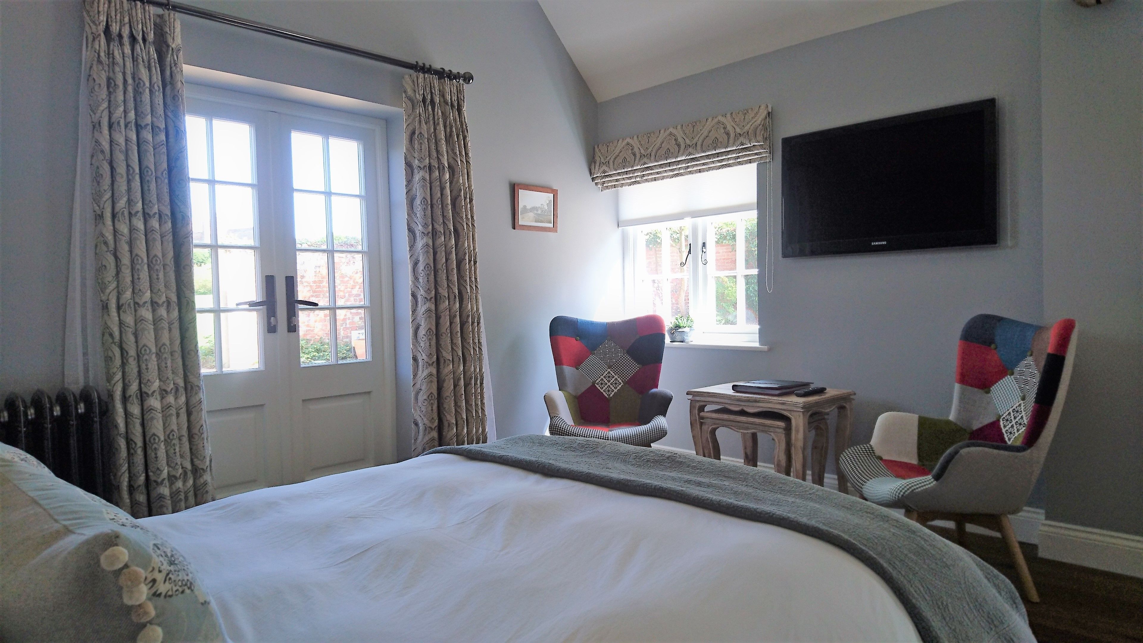 A bedroom with a large bed, a chair, a small table, a TV, and a window with curtains.