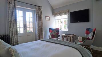 A bedroom with a large bed, a chair, a small table, a TV, and a window with curtains.