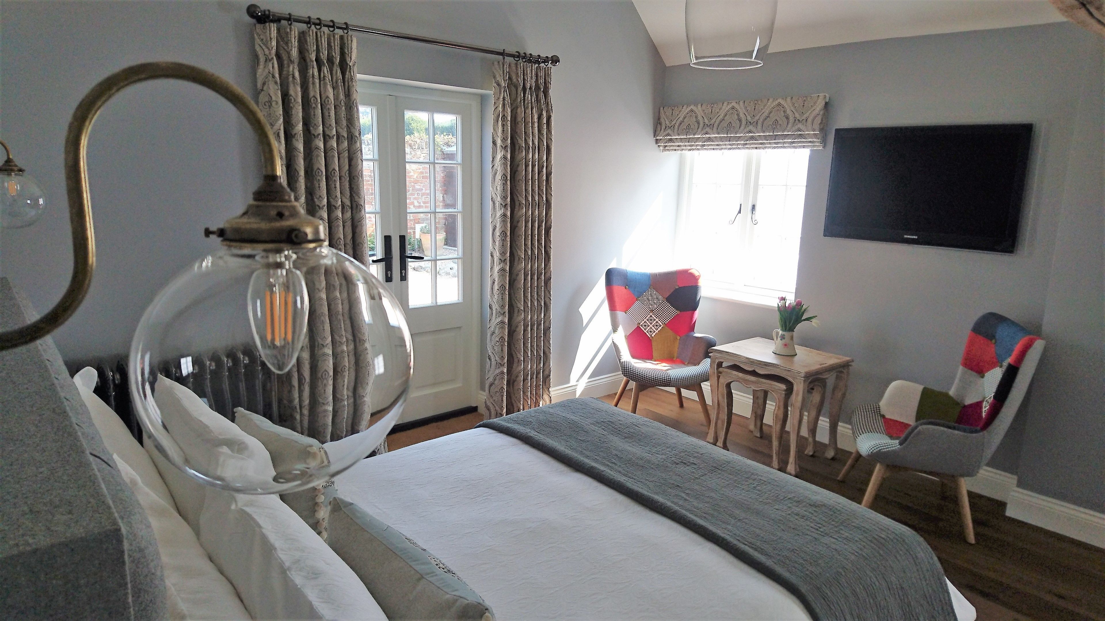 A bedroom with a bed, a desk, two chairs, a television, and a window with curtains.