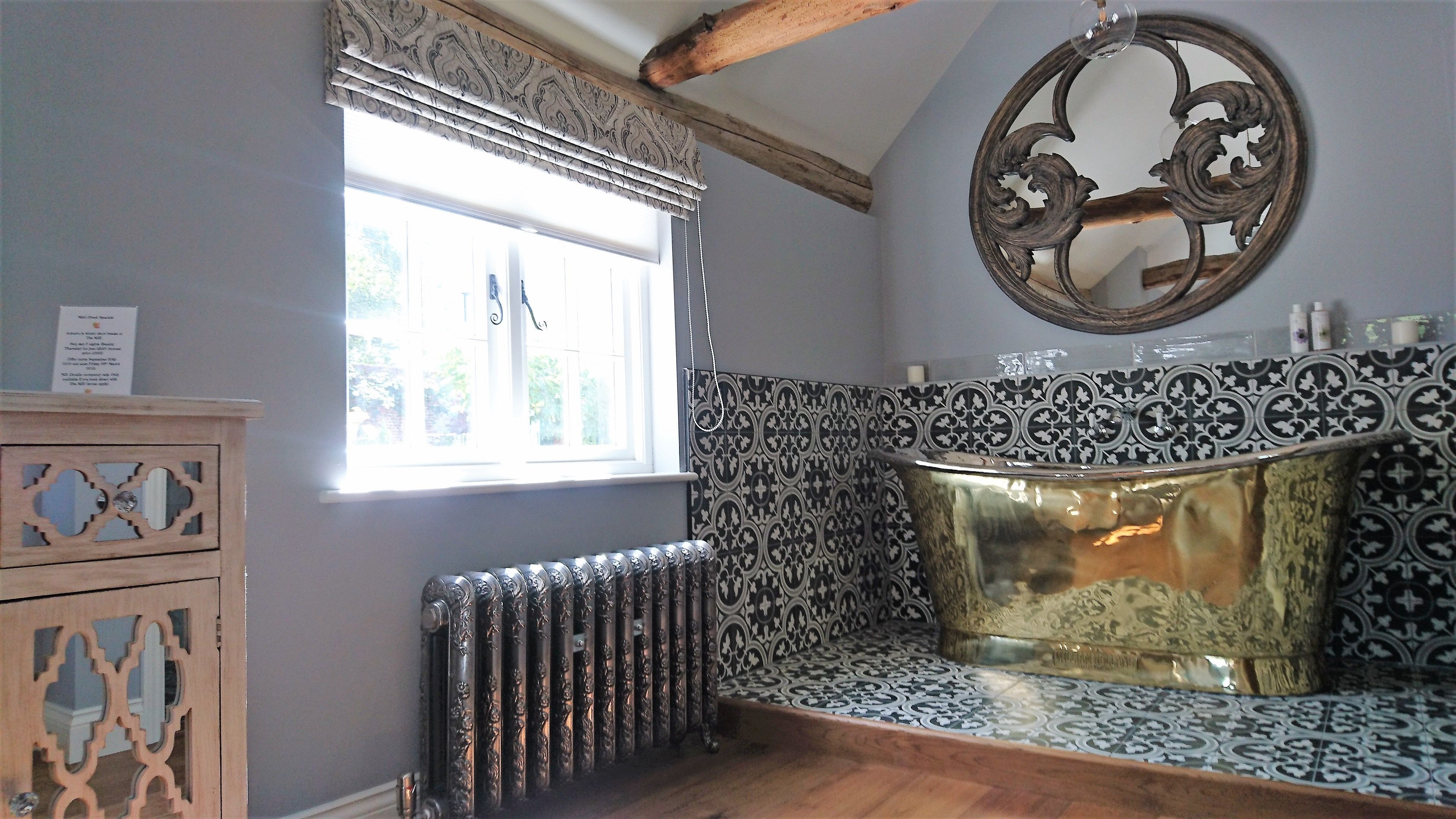 A bathroom with a radiator, patterned tiles, a wooden cabinet with glass doors, and a decorative mirror.